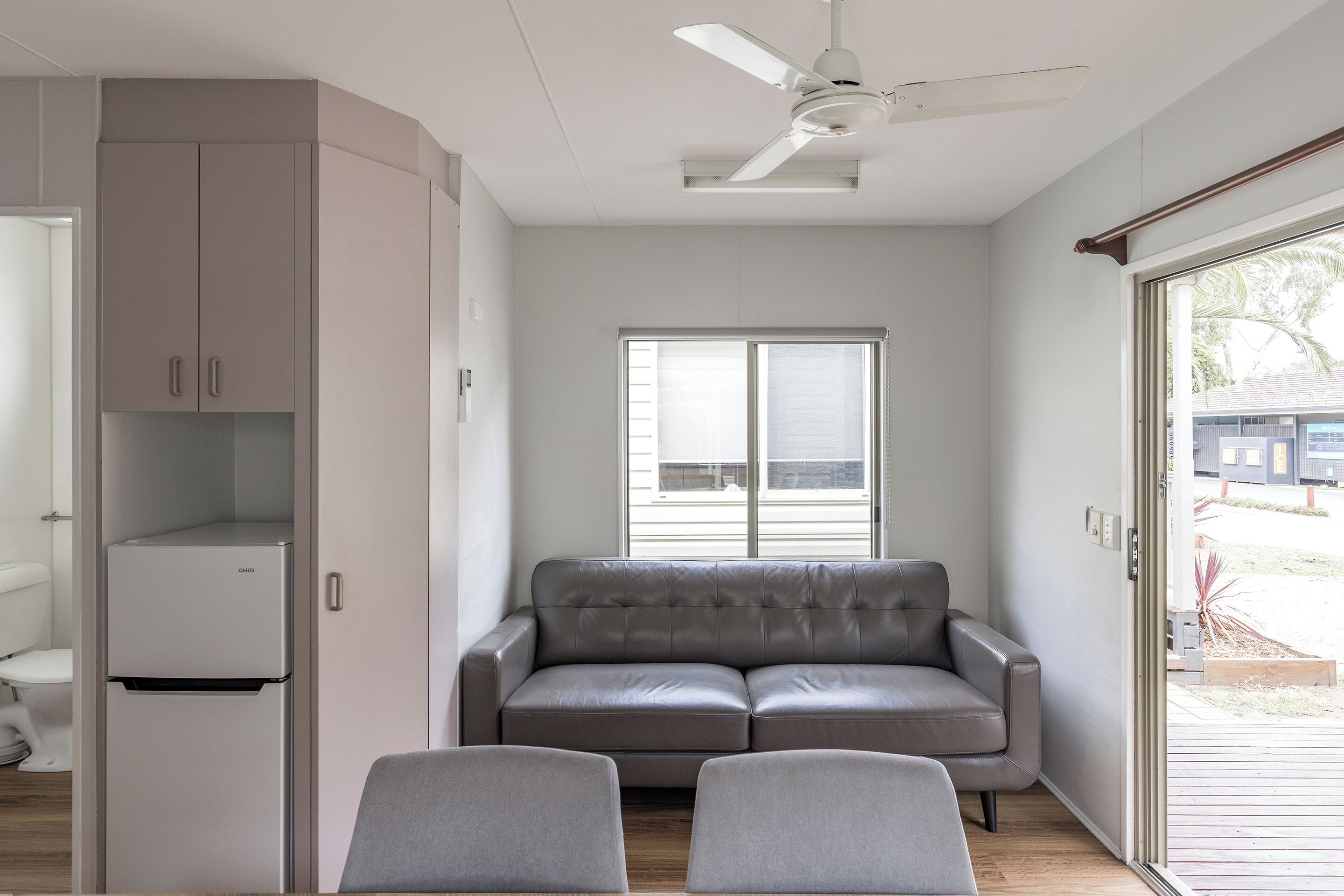 Ein modernes Wohnzimmer mit grauem Sofa, einem kleinen Tisch und einem eingebauten, weißen Kühlschrank.