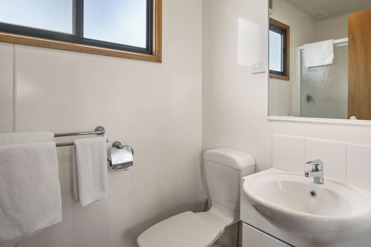 Une salle de bain équipée de toilettes, d’un lavabo, d’un porte-serviettes et d’une fenêtre.
