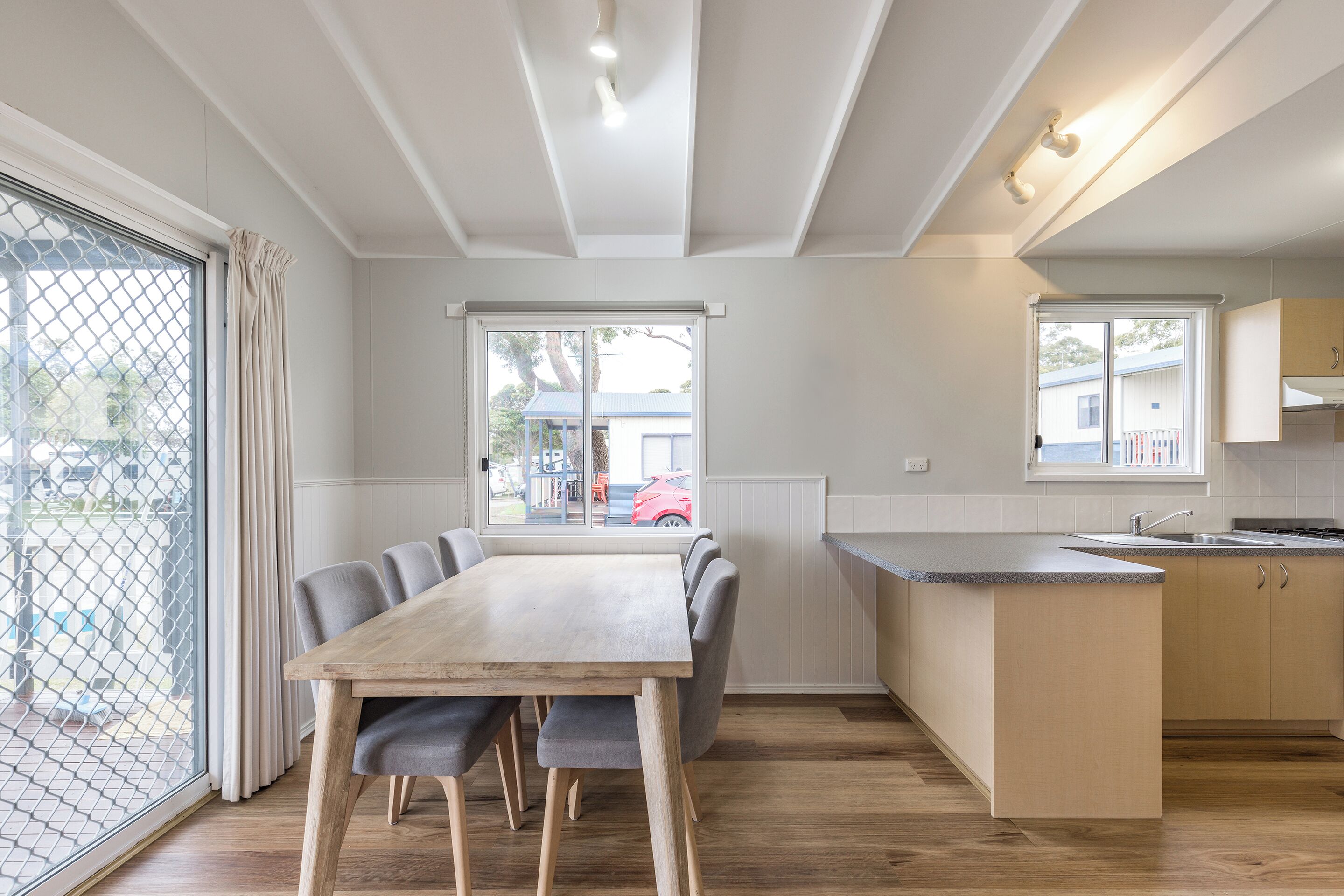 A modern kitchen with a wooden dining table, grey chairs, and a small island with a sink.