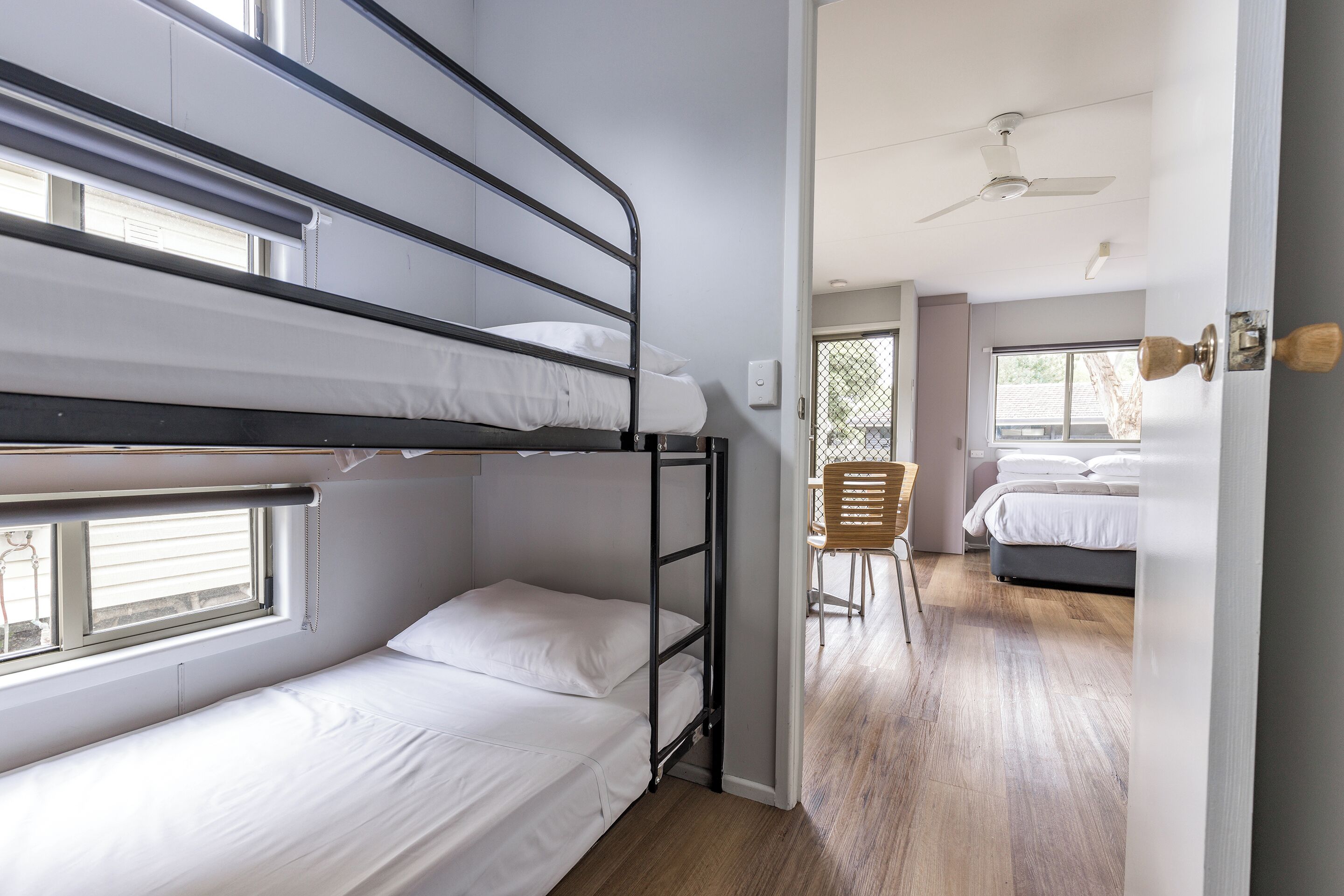 Habitación con literas, una ventana, una puerta que da a otra habitación y un ventilador de techo.