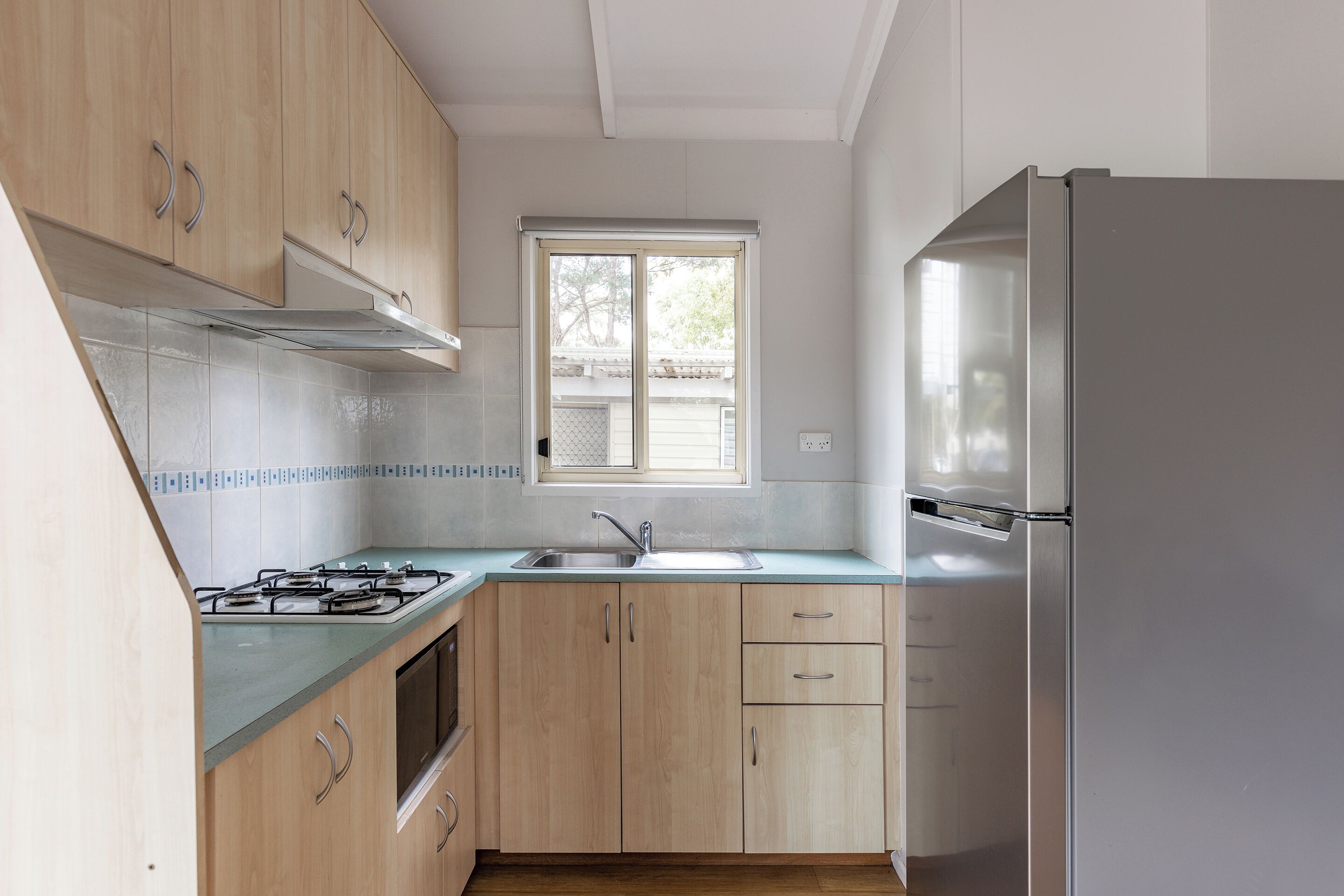 A modern kitchen with wooden cabinets, a stainless steel refrigerator, a gas stove, and a window providing natural light.