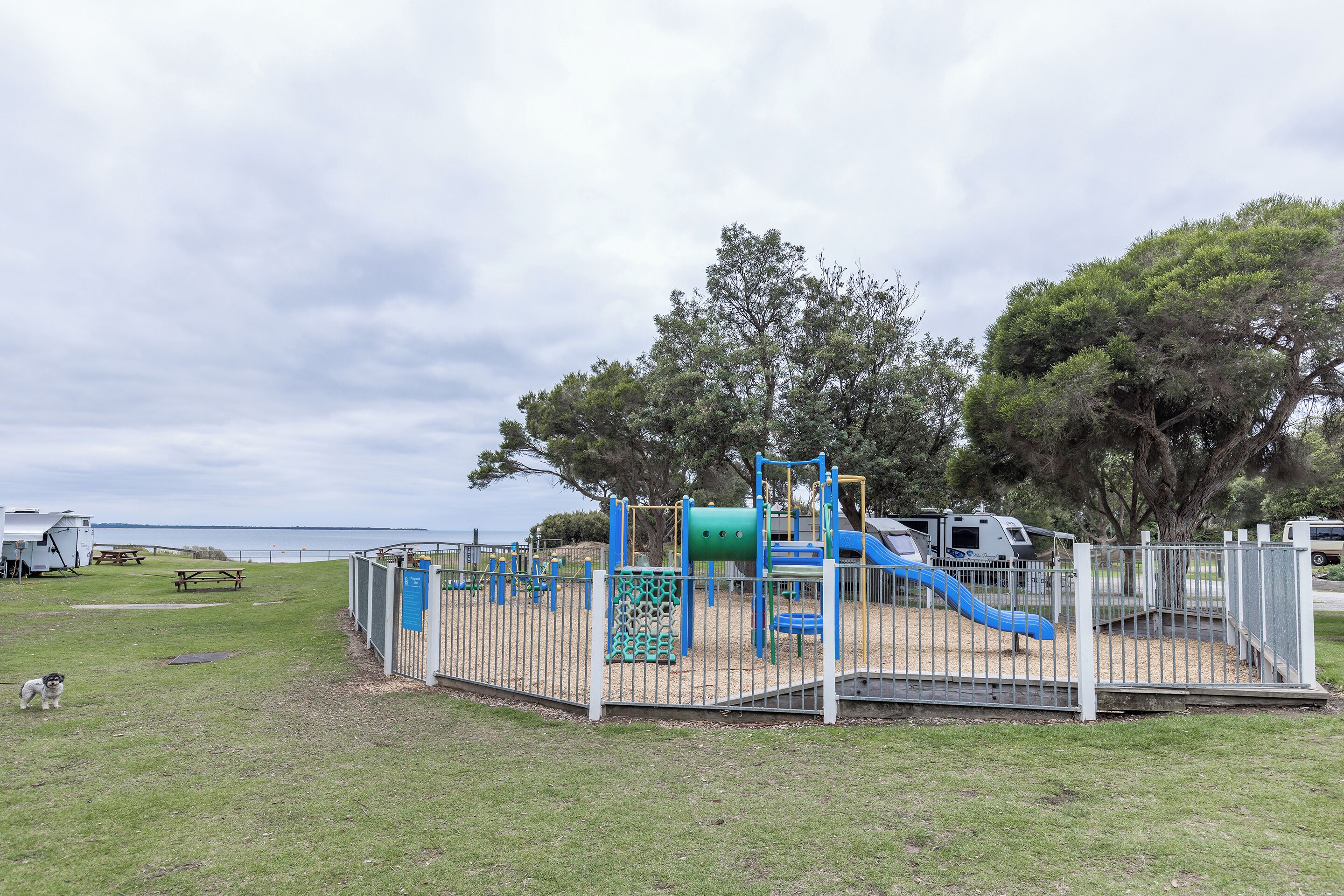 A playground with a slide and climbing structures, a picnic table, and a fenced area.