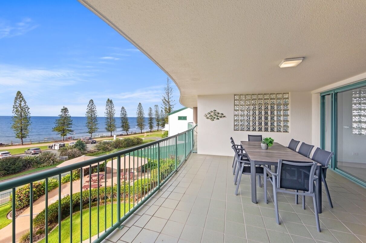 A balcony with a dining table and chairs, a view of the sea, and a patterned wall.