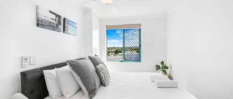 A modern bedroom with a bed, a ceiling fan, a window with a view, and a small plant.
