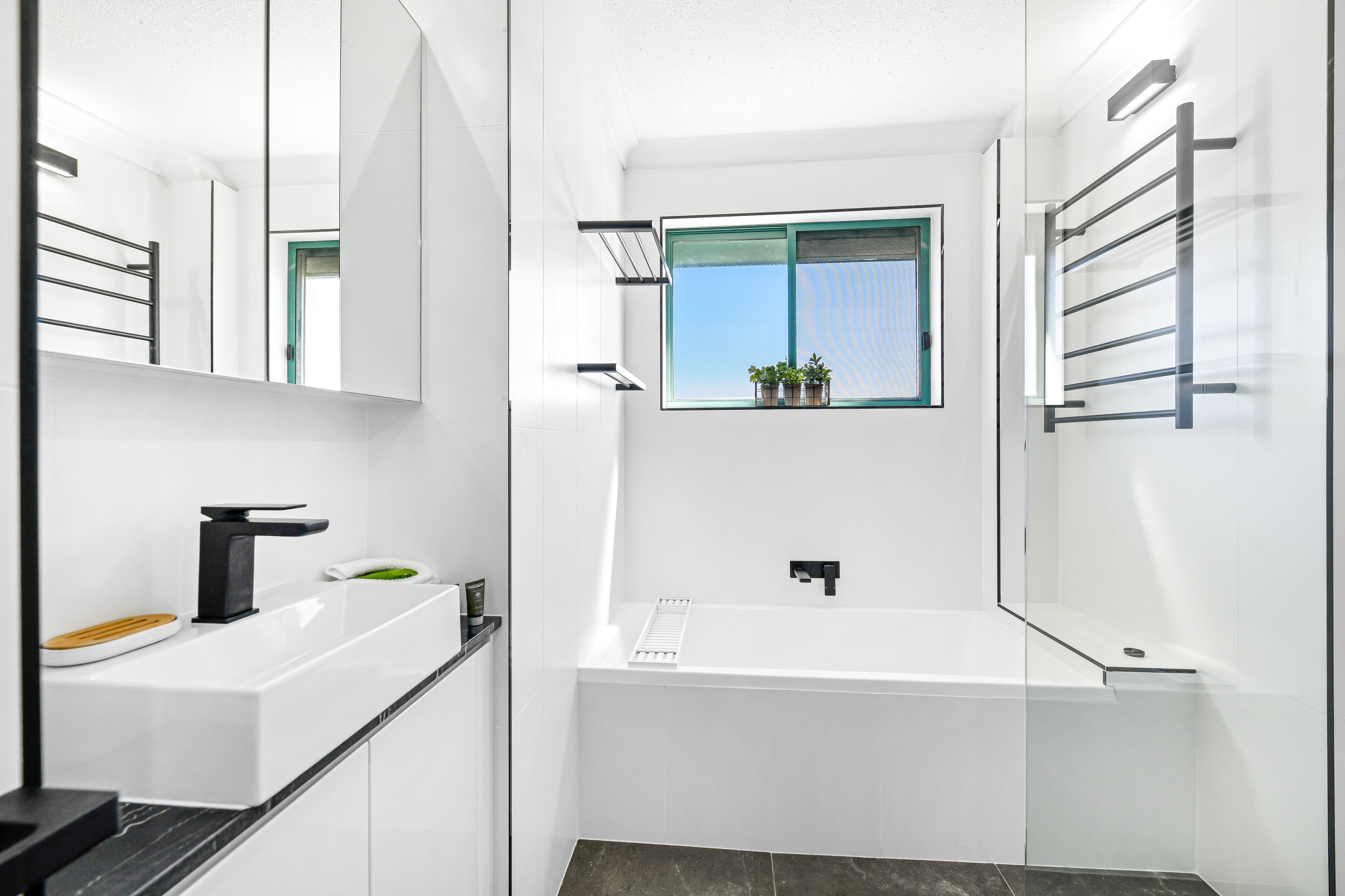 Un baño moderno con bañera, lavamanos y ventana con plantas.