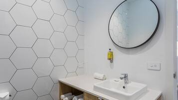 A bathroom with a hexagonal tile wall, a round mirror, a white sink, and a towel rack.