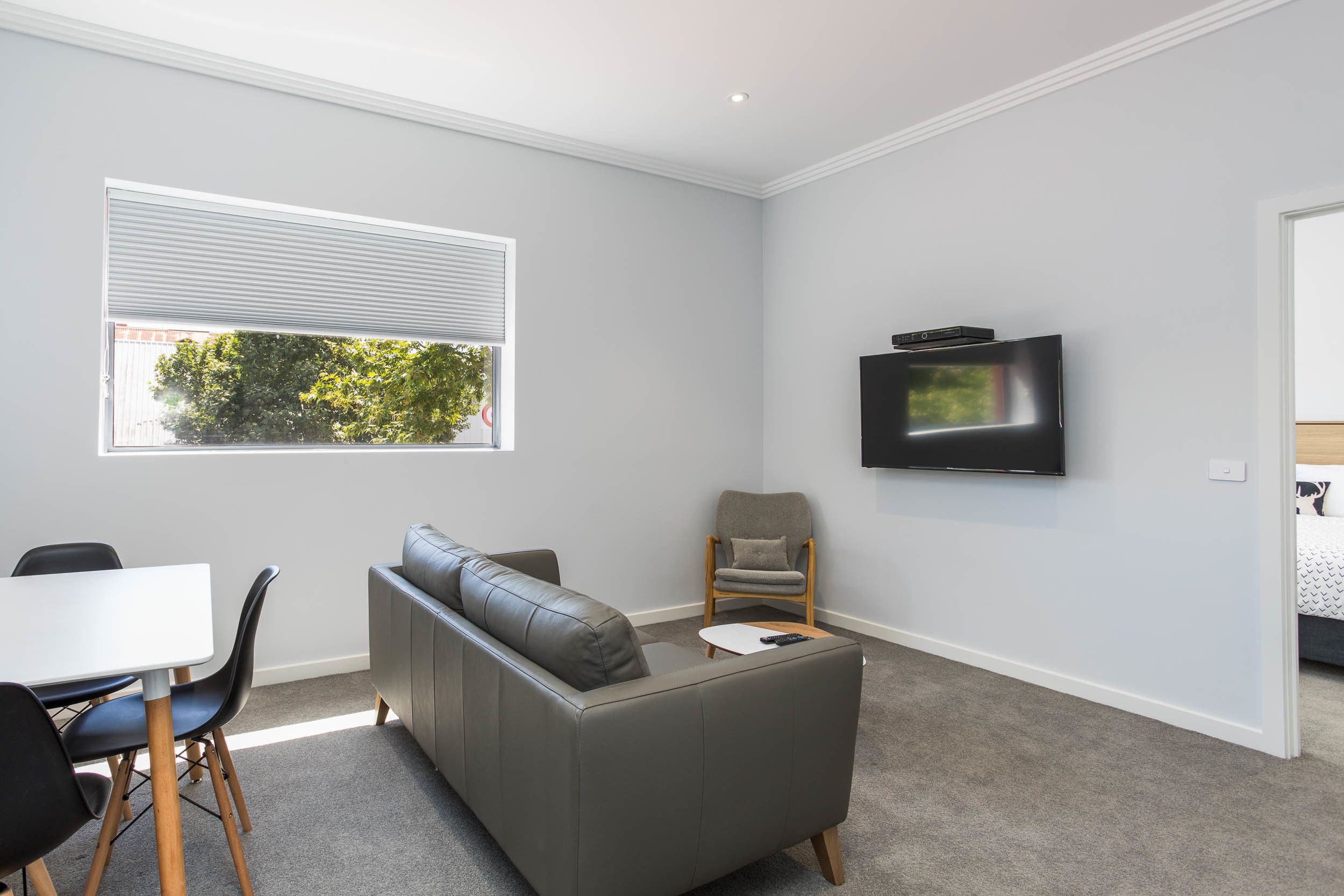 Een moderne woonkamer met een grijze bank, een witte tafel en een aan de muur bevestigde televisie.