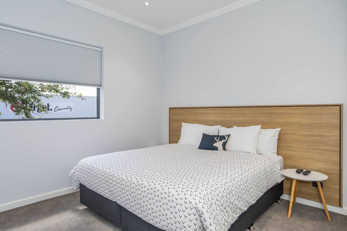 A bedroom with a bed, a bedside table, a window, and a view of a building outside.