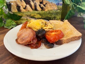 A plate of breakfast food including toast, eggs, bacon, mushrooms, and tomatoes.