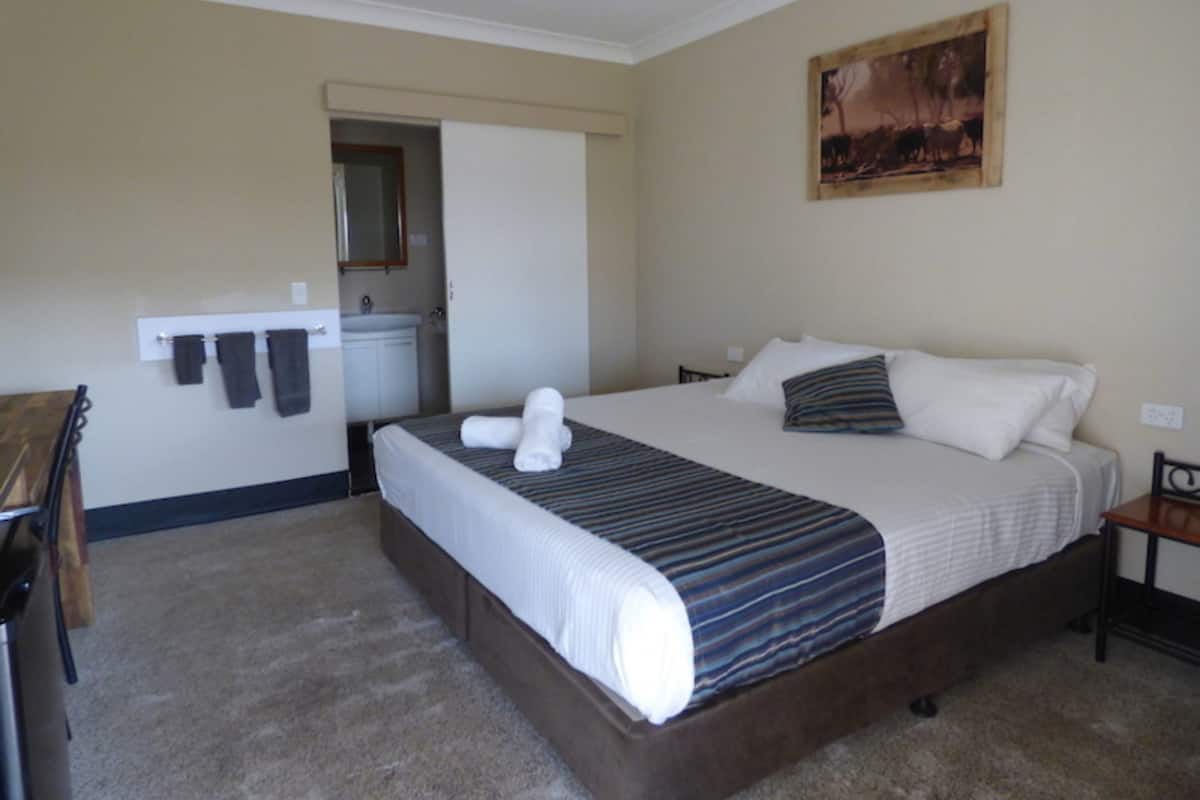 A hotel room with a bed, a desk, a chair, a bathroom, and a painting on the wall.