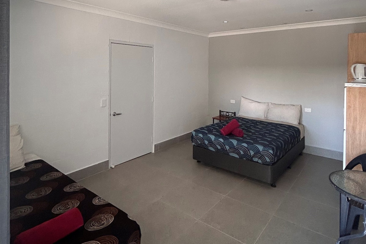 A spacious room with a large bed, a small table, and a door.