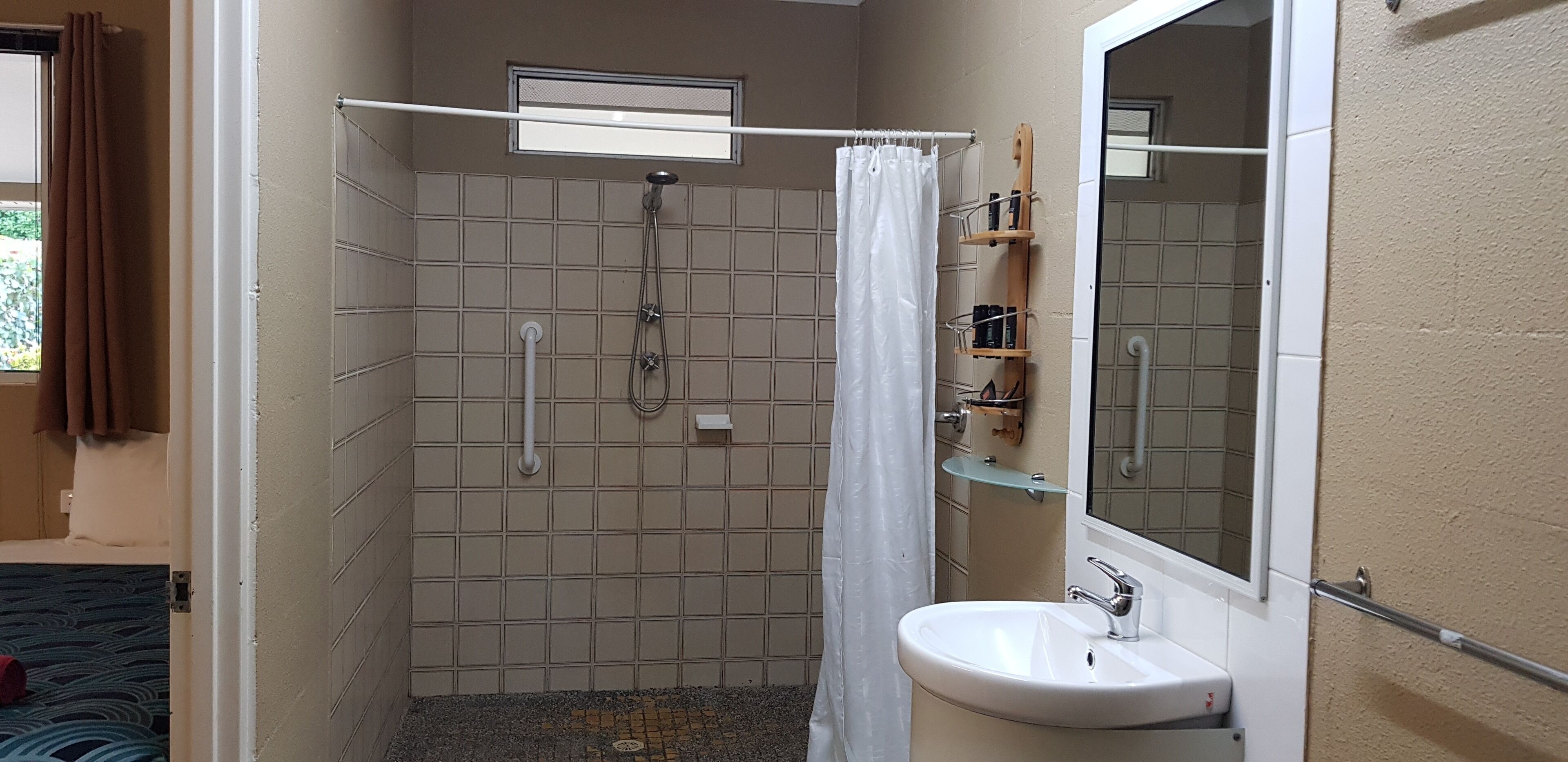 A small bathroom with a shower, a sink, and a mirror.