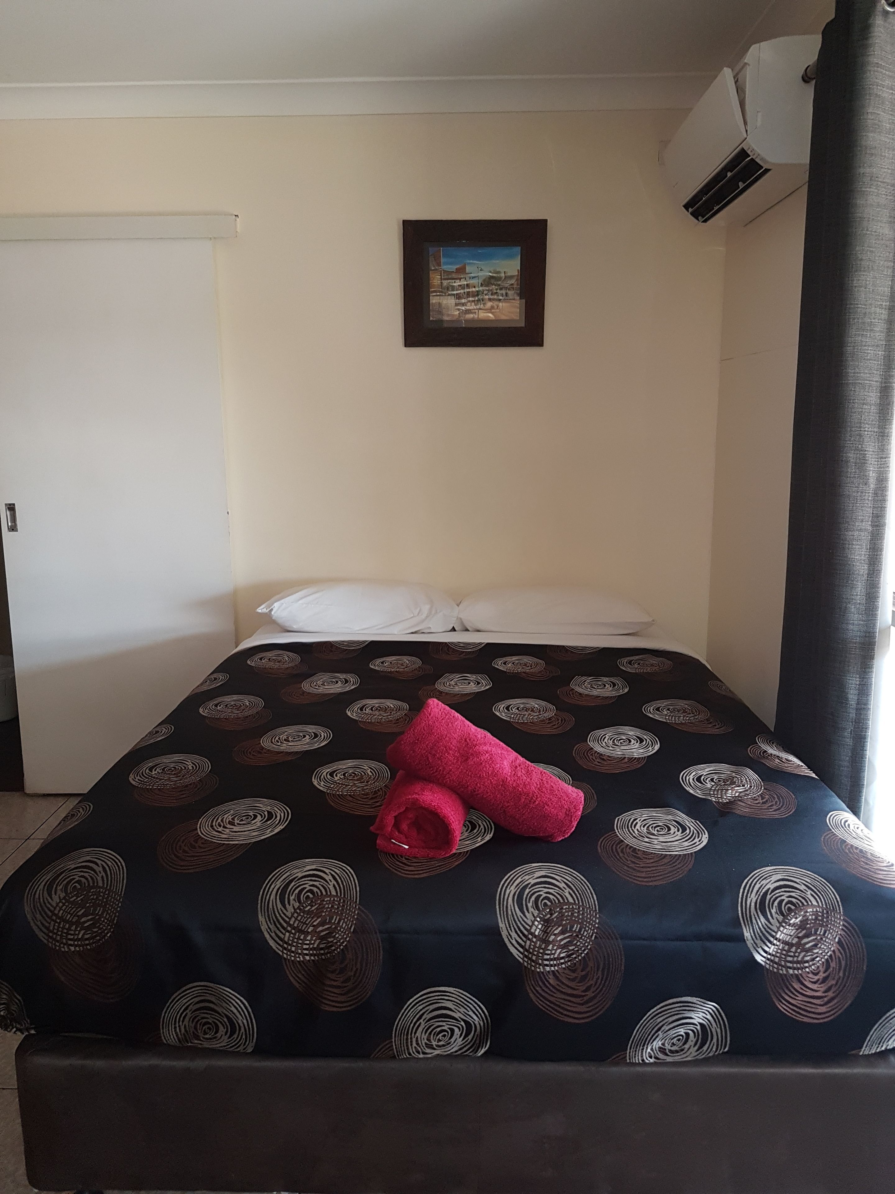 Una habitación de hotel con una cama, un cuadro en la pared y un equipo de aire acondicionado.