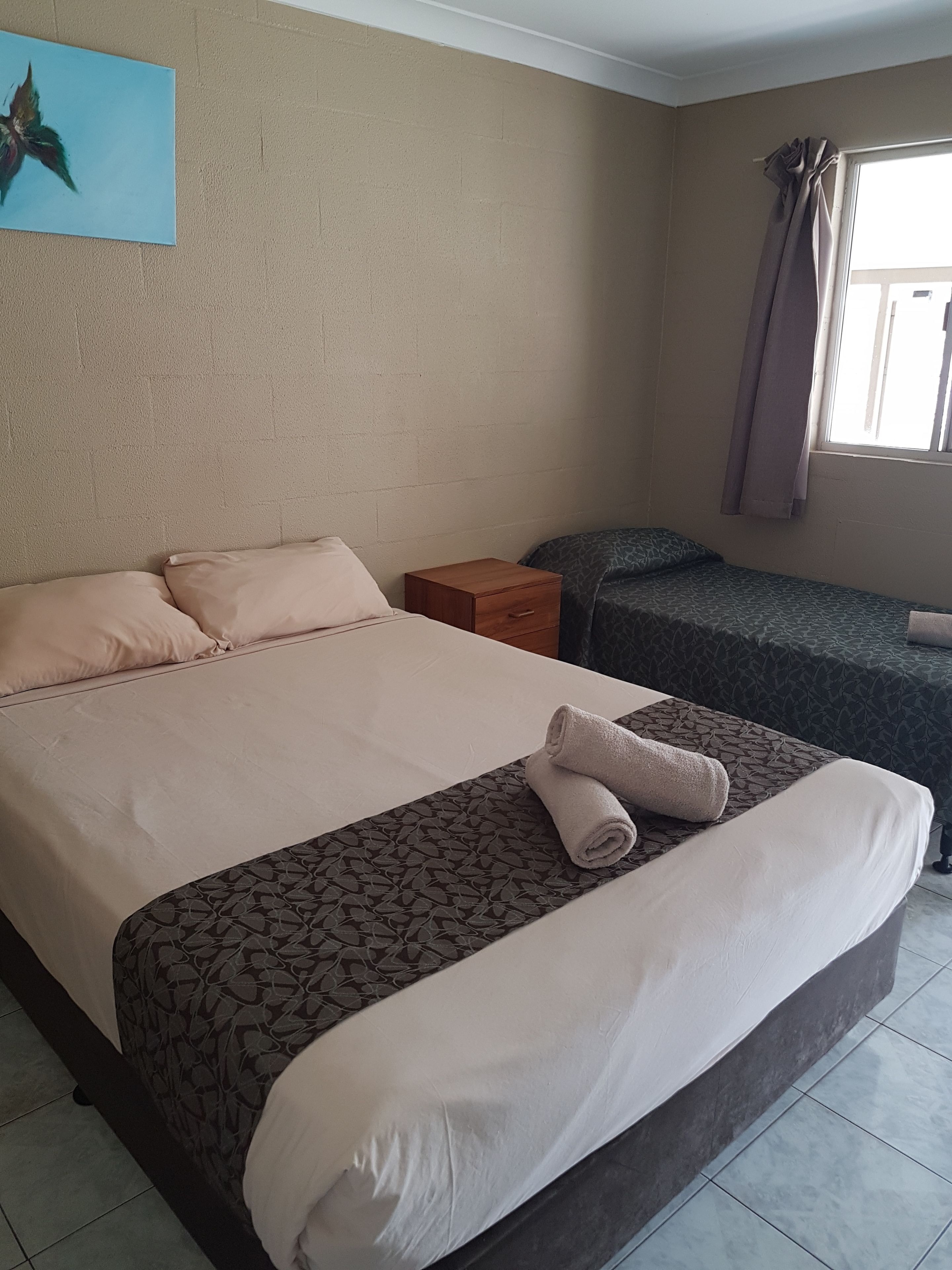 Ein Hotelzimmer mit einem großen Bett, einem kleineren Bett, einem Nachttisch und einem Fenster mit Vorhängen.