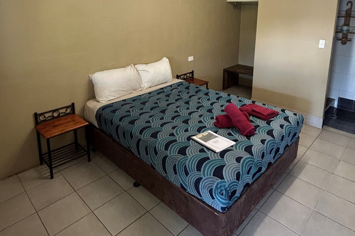 A standard hotel room with a single bed, a nightstand, a small table, and a bathroom visible through an open door.