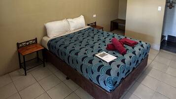 Habitación de hotel estándar con una cama individual, una mesita de noche, una pequeña mesa y un baño visible a través de una puerta abierta.