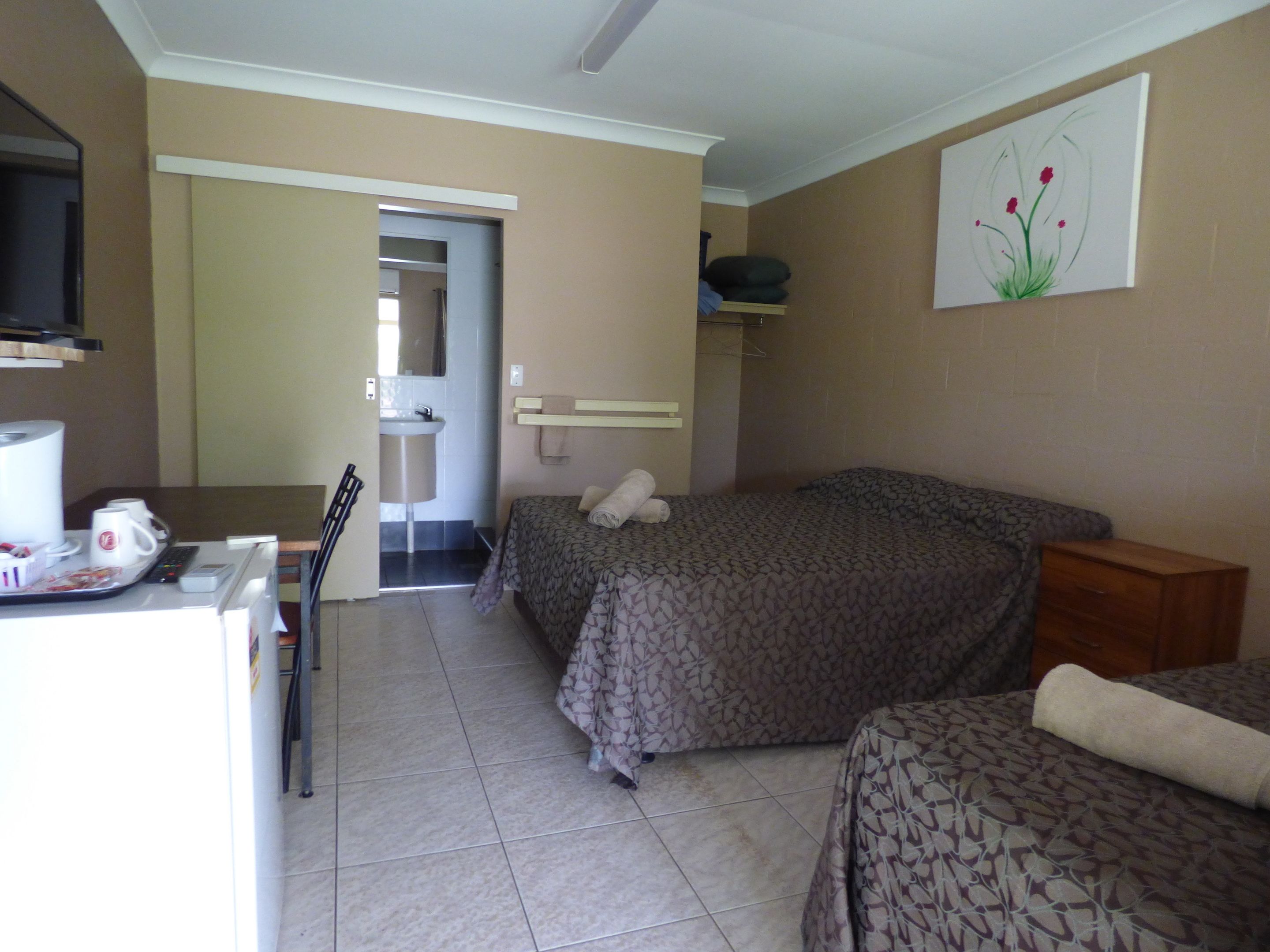 A hotel room with a bed, a desk with a telephone and a coffee maker, a bathroom with a sink, and a painting on the wall.