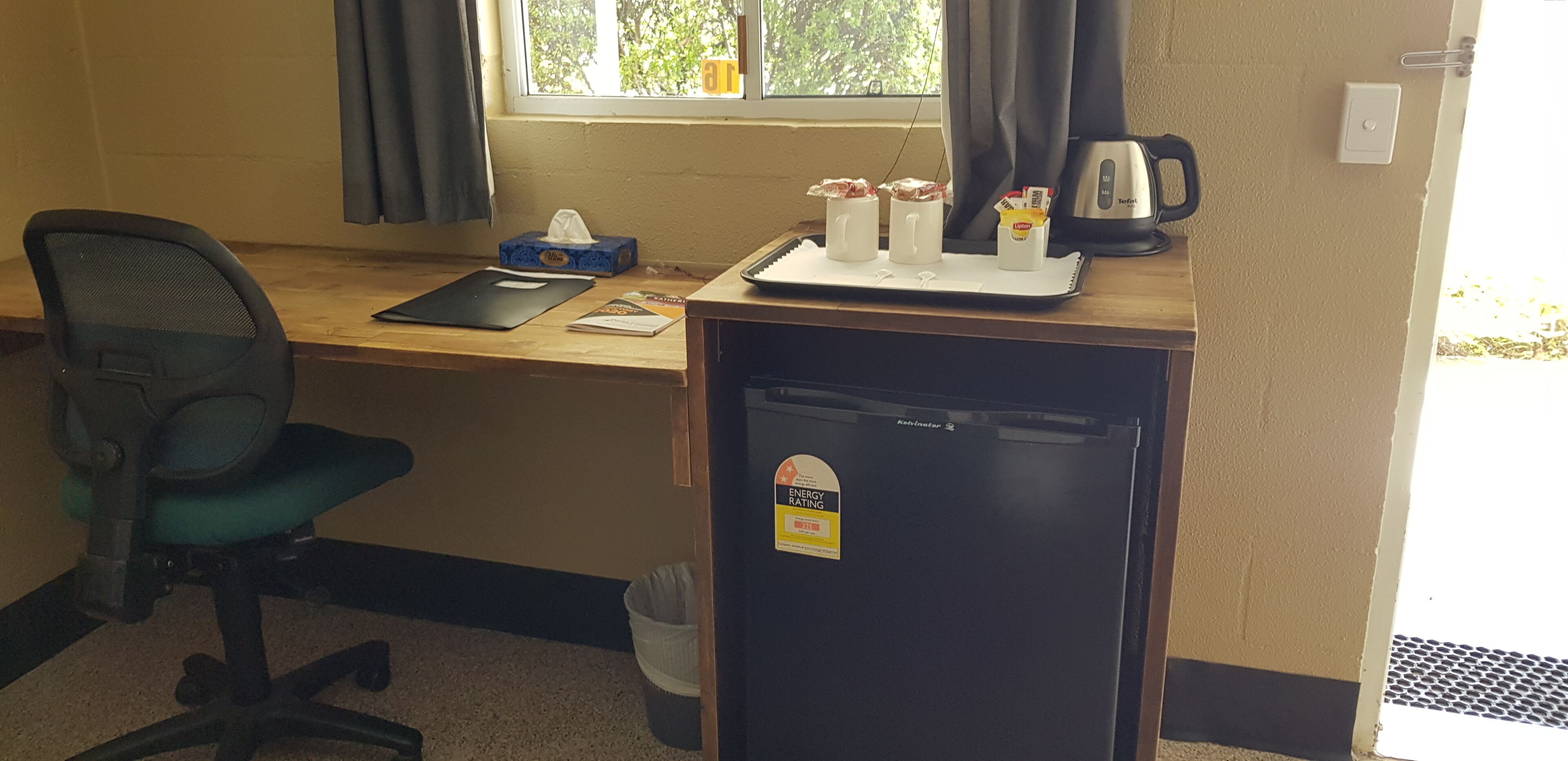 Een compacte kitchenette met een koelkast, een koffiezetapparaat en een klein dienblad met etenswaren.