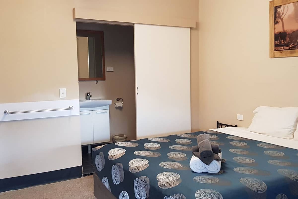 A hotel room with a bed, a nightstand, a bathroom with a towel rack, and a painting on the wall.