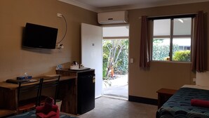 A compact hotel room with a bed, a desk with a chair, a small refrigerator, a TV mounted on the wall, and a window with curtains.