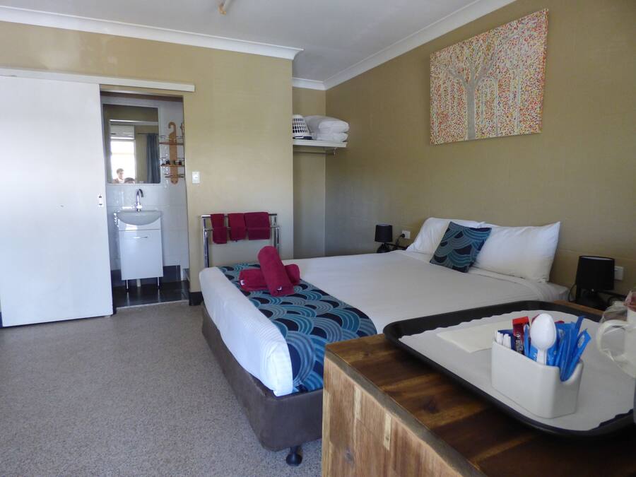 Une chambre d’hôtel comprenant un lit, une table de chevet et une salle de bain avec un lavabo et un miroir.