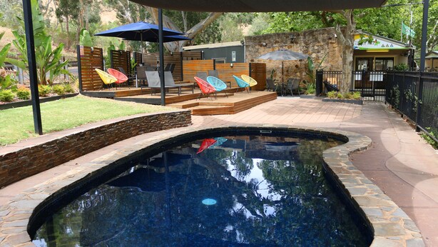 A swimming pool with a stone border, surrounded by a patio area with lounge chairs and umbrellas.