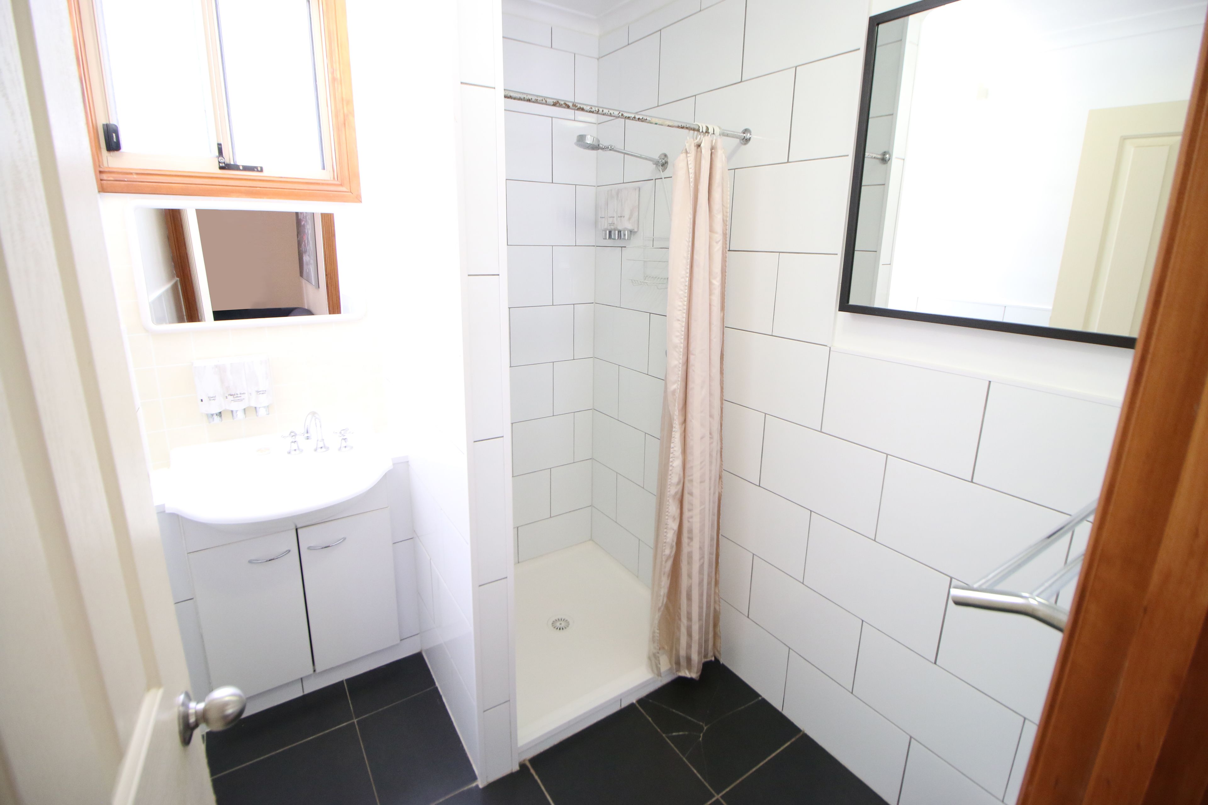 A bathroom with a white sink, a mirror, a shower with a beige curtain, and a tiled floor.