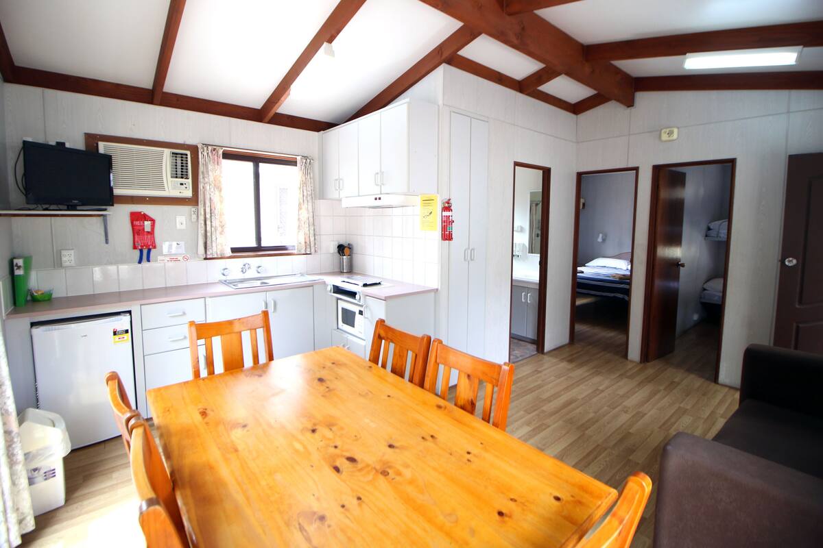Een kleine keuken met witte kasten, een houten eettafel en een televisie.