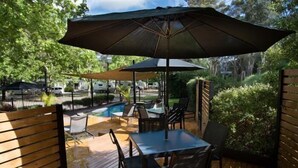 An outdoor deck with a pool, tables, and chairs, surrounded by greenery.
