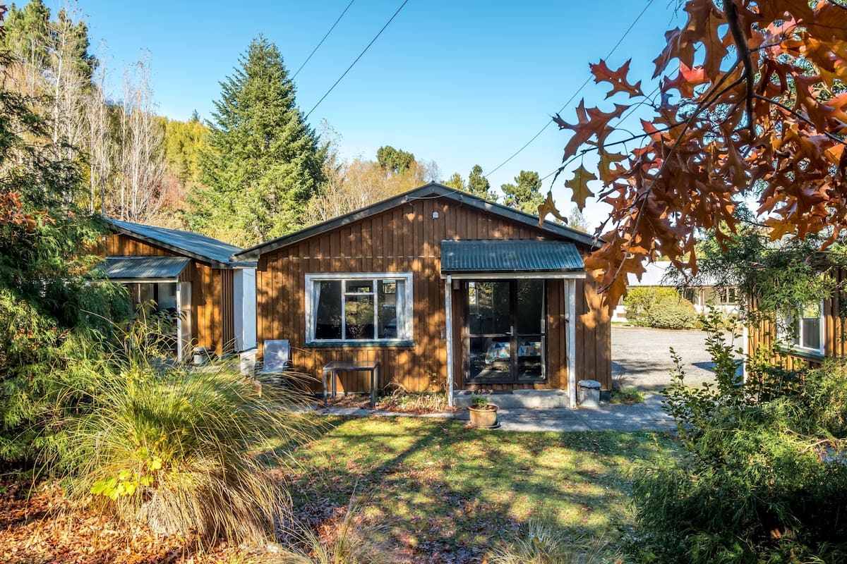 A wooden cabin with a porch, surrounded by trees and a clear sky.
