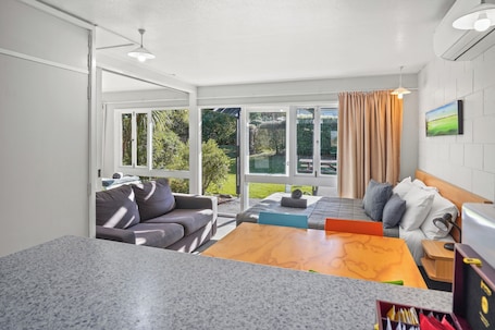 A modern room with a large sliding glass door leading to a garden, a sofa, a wooden coffee table, and a bed with pillows.. Alpine Adventure Holiday Park