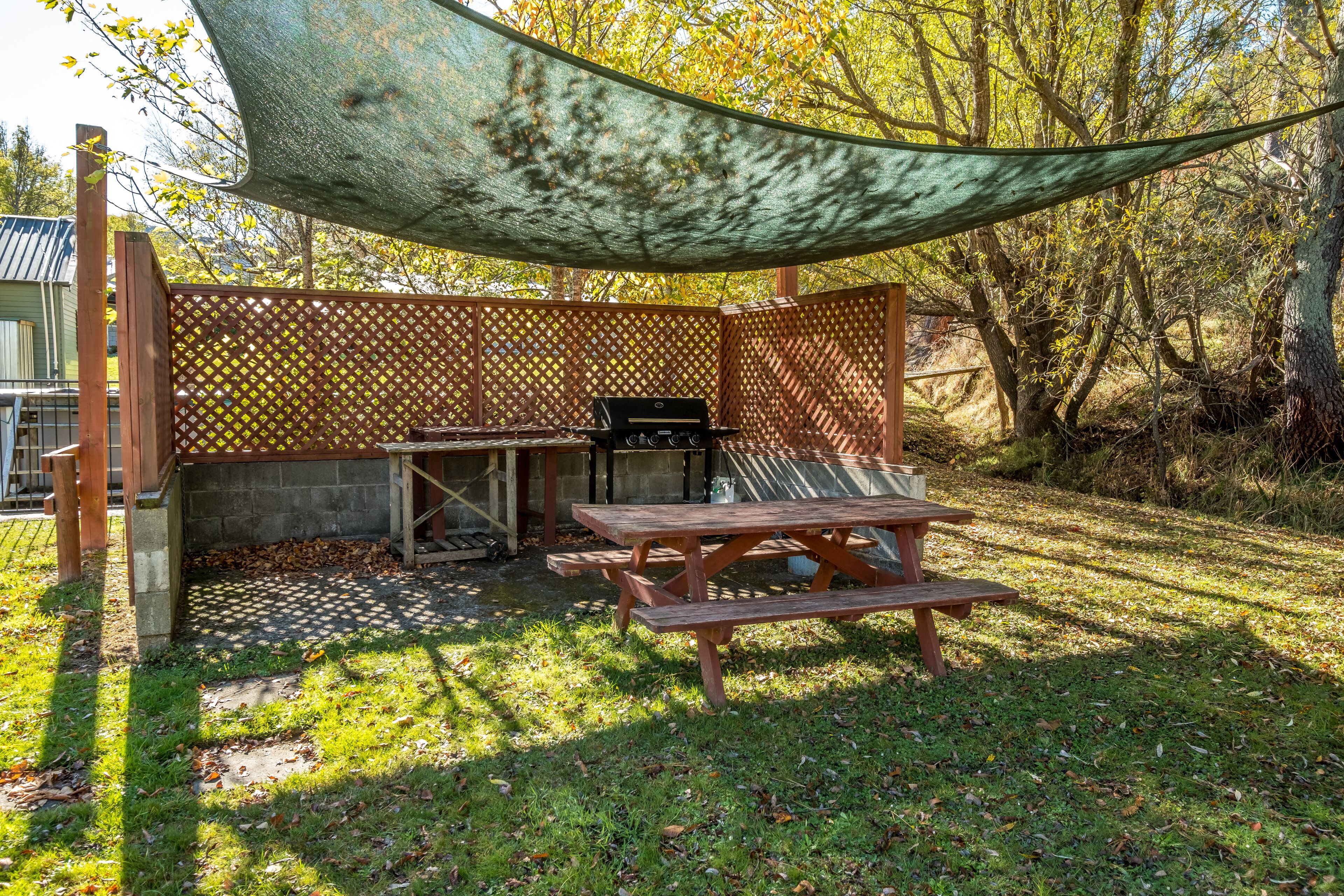 An outdoor patio with a grill, wooden table, and a shaded area.