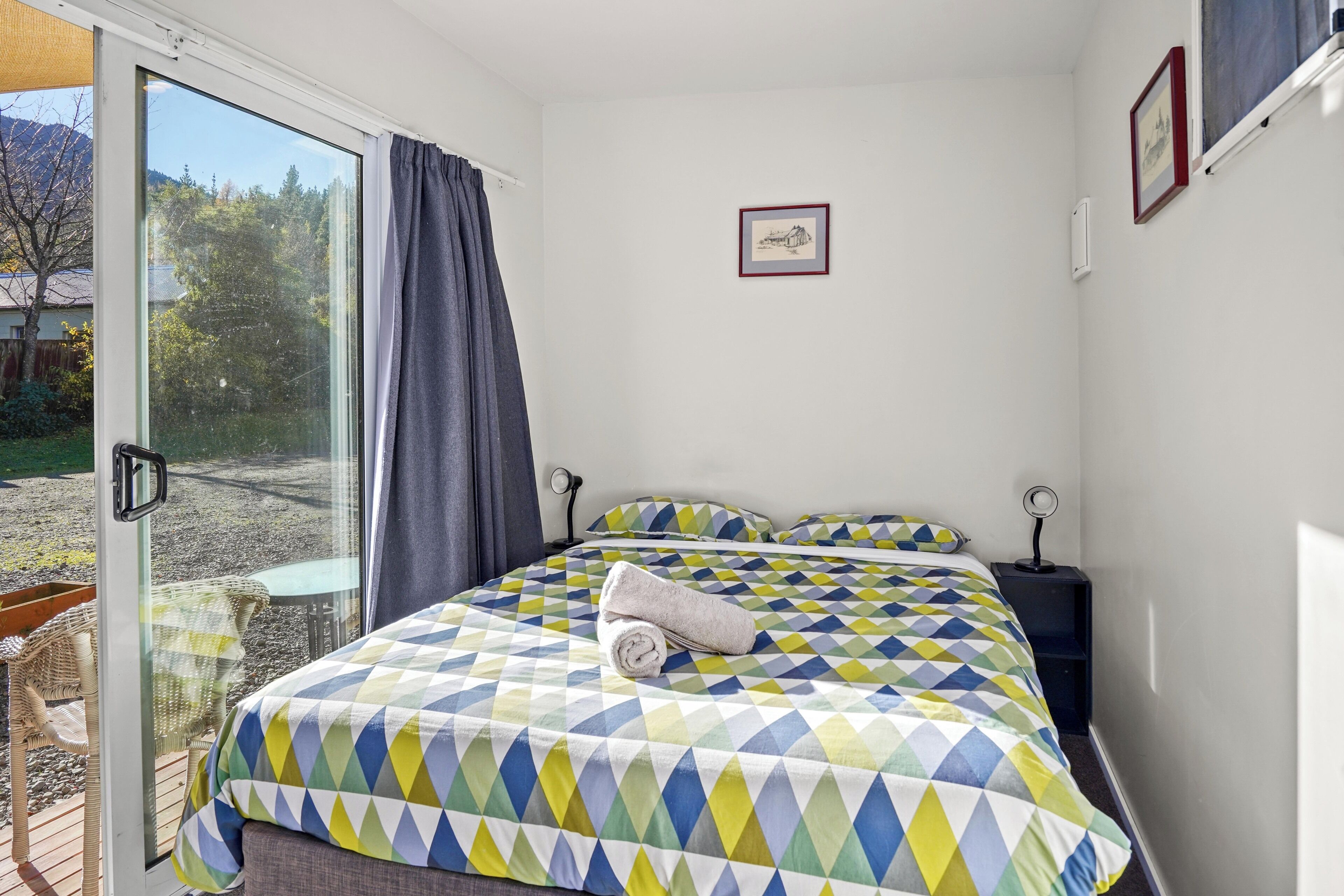 Un dormitorio con una cama grande, una ventana, un cuadro enmarcado y una mesita.
