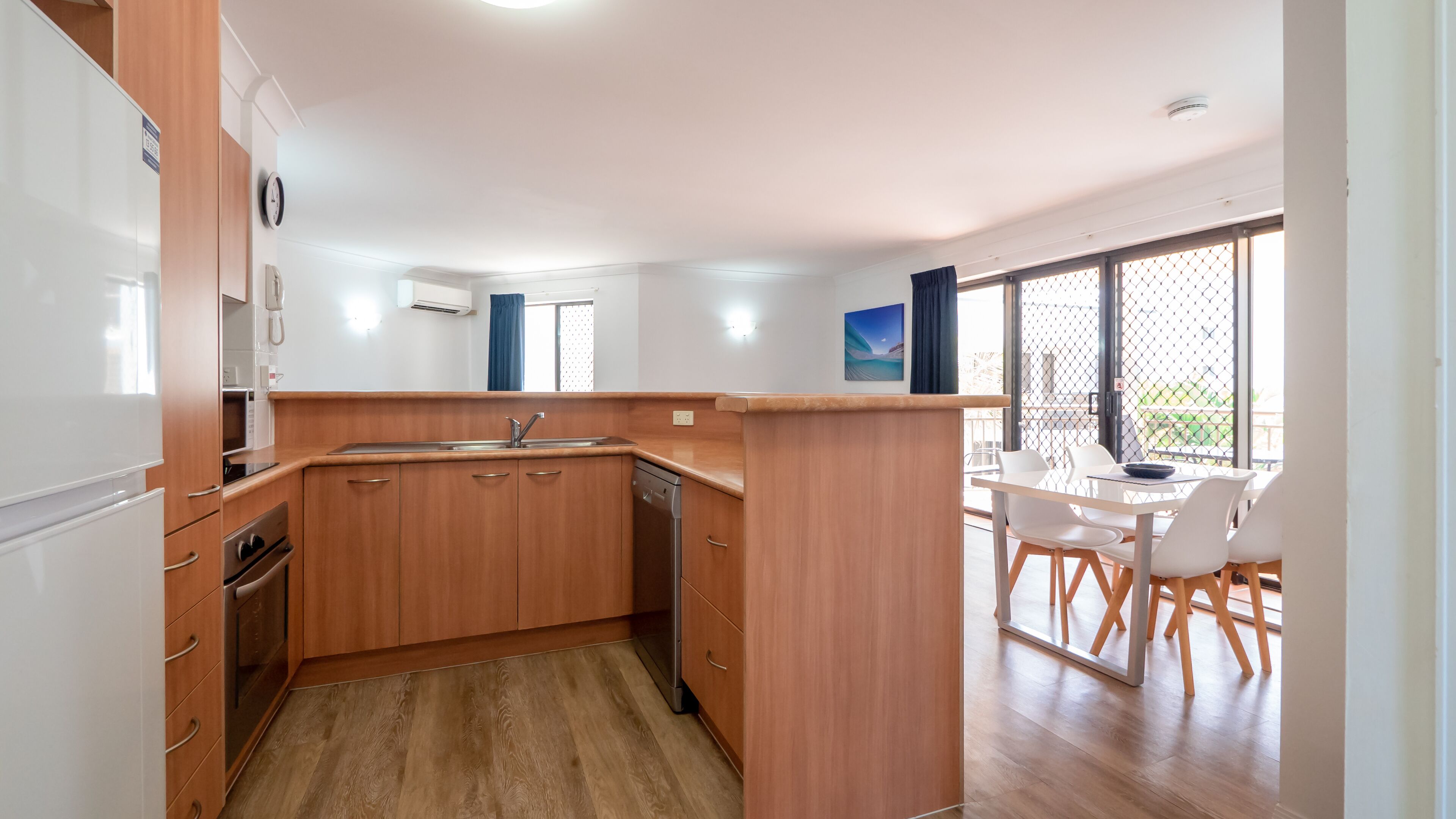A modern kitchen with wooden cabinets, a built-in dishwasher, and a dining area with a table and chairs.
