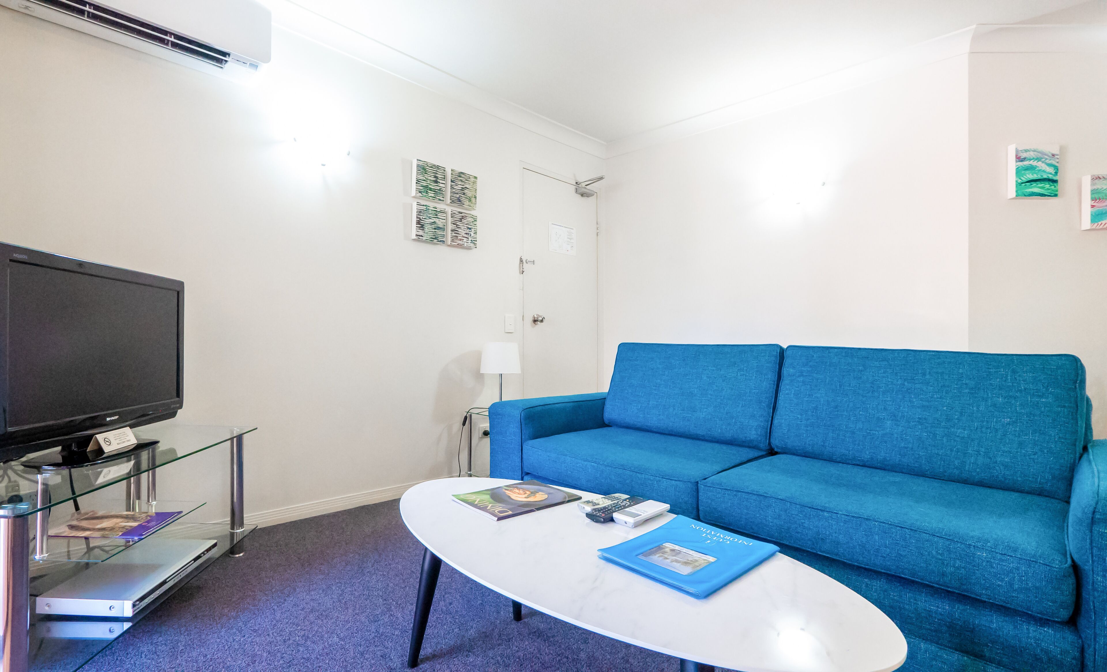 Una sala moderna con un sofá azul, un televisor de pantalla plana y una mesa de centro de vidrio.