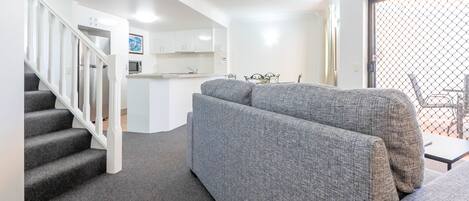 Een moderne woonkamer met een grijze bank, een trap, een keukenhoek en uitzicht door een gaasdeur.