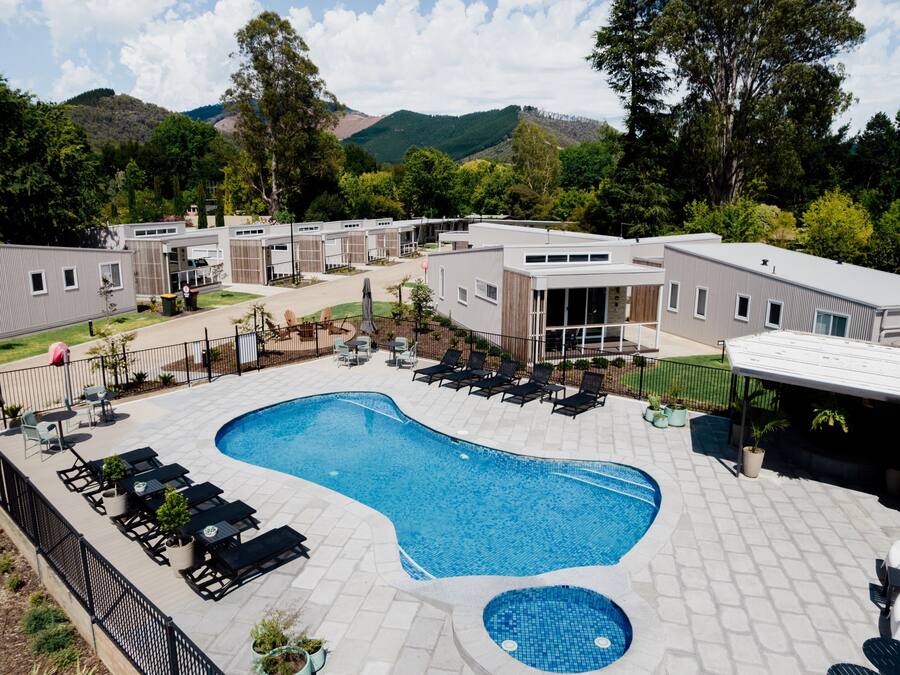 Una piscina con sillas de descanso y un patio cubierto, rodeada de edificios y árboles.