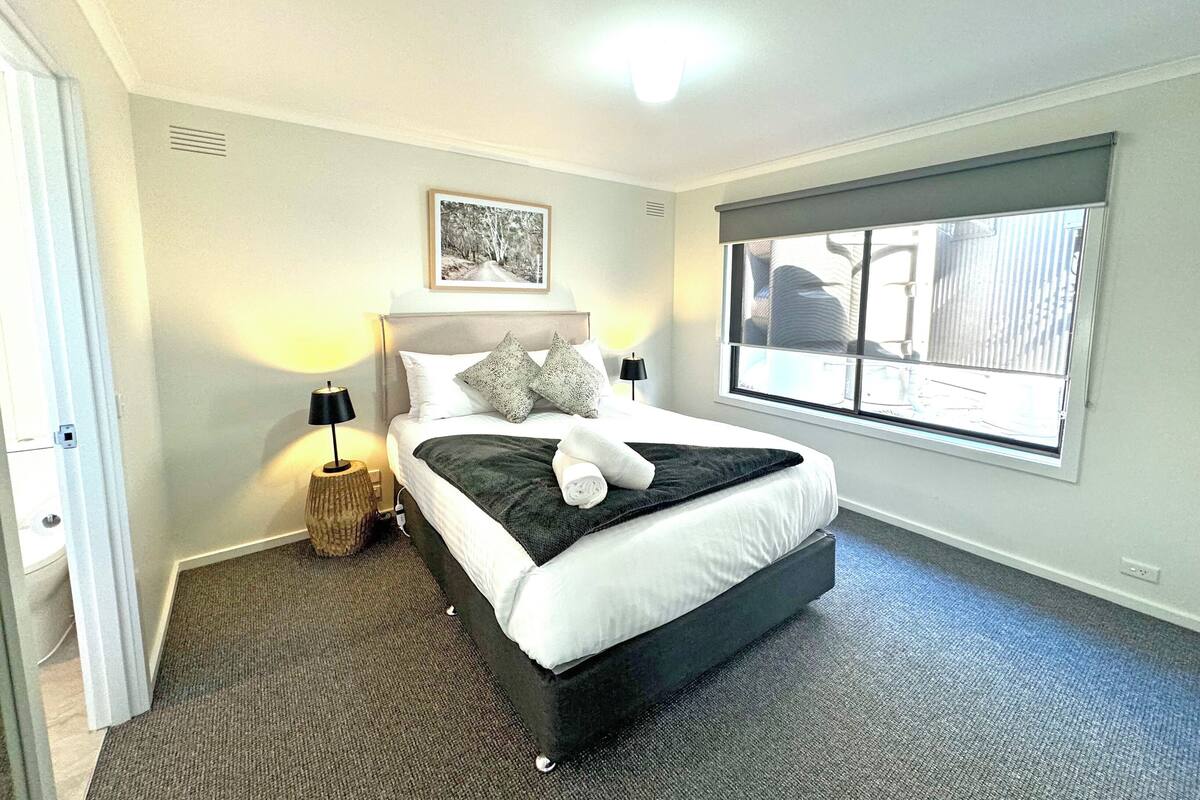 Quarto de hotel bem organizado, com uma cama grande, luminária na cabeceira, quadro na parede e janela com vista.