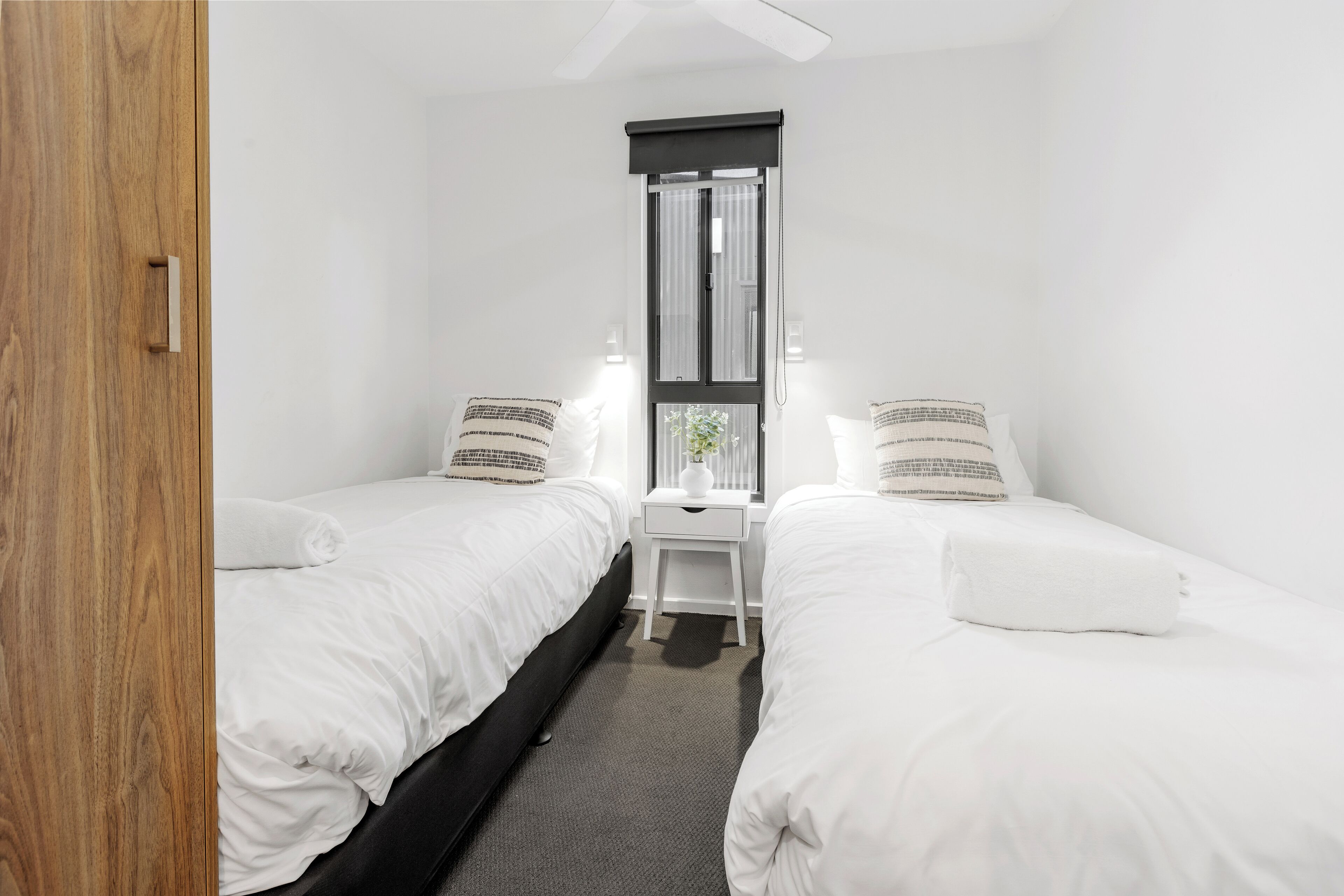 A small, clean room with two single beds, a small desk, and a window with curtains.