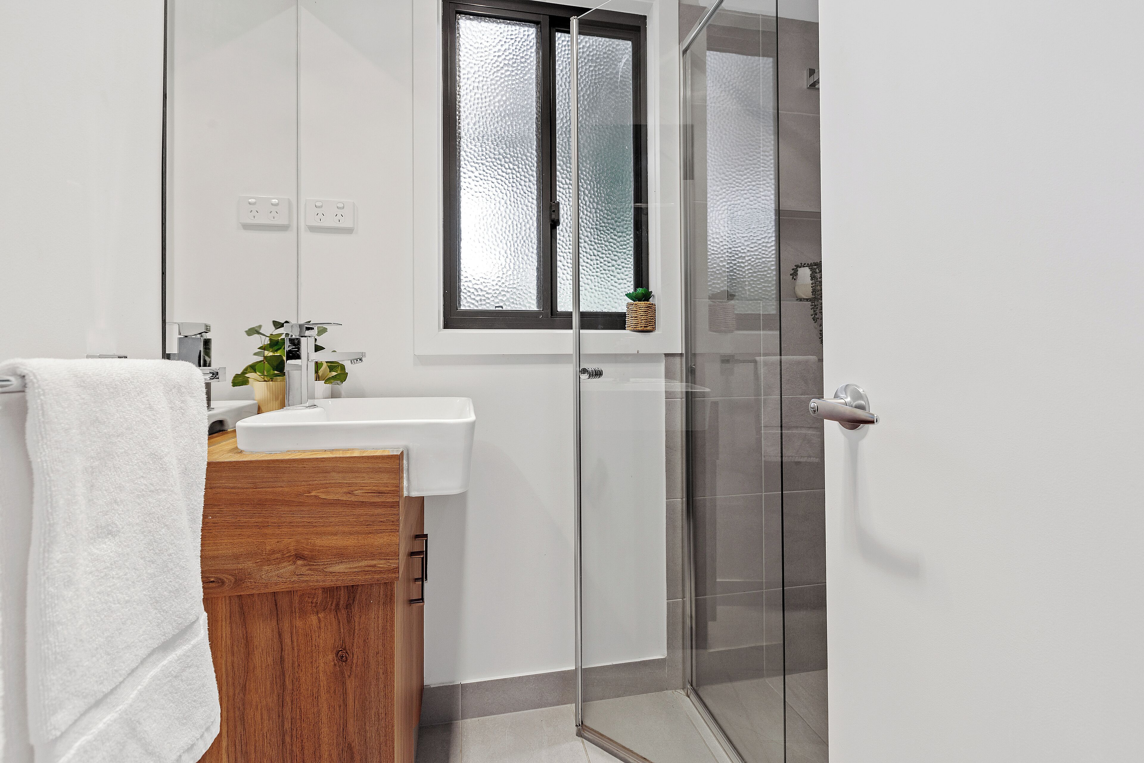 A modern bathroom with a glass shower enclosure, a wooden vanity, and a white sink.