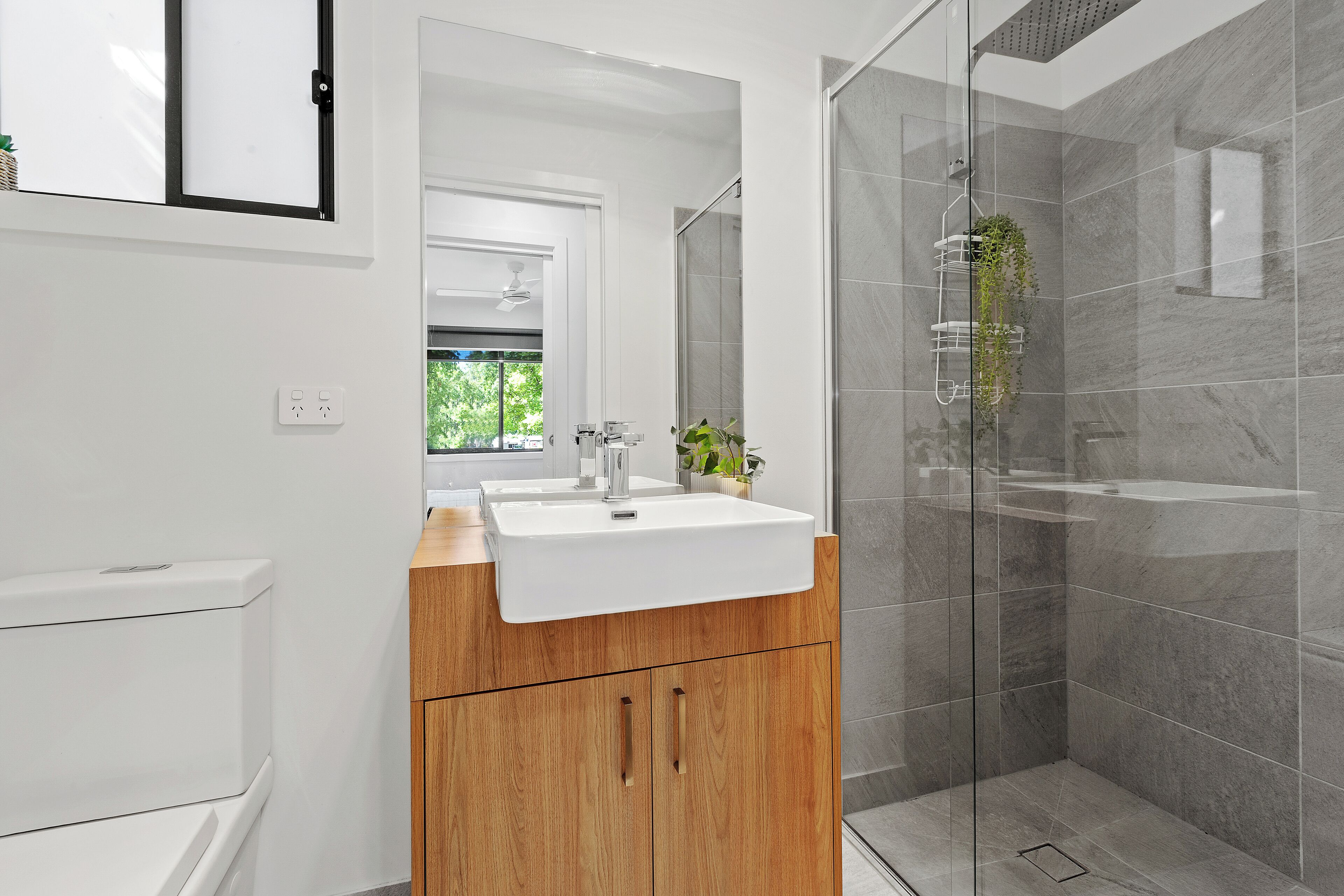 A modern bathroom with a wooden vanity, a white sink, and a glass-enclosed shower.