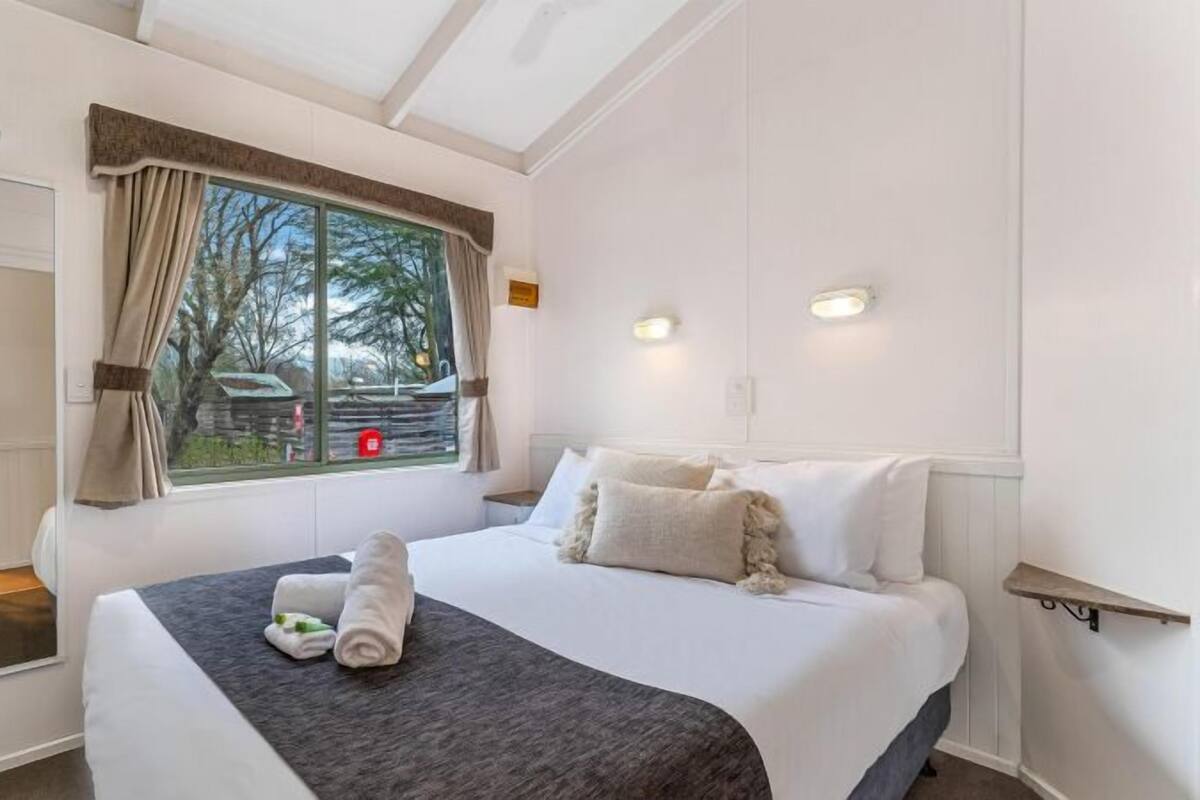 Quarto de hotel com uma cama grande, janela com cortinas, mesa de cabeceira e vista para o exterior.