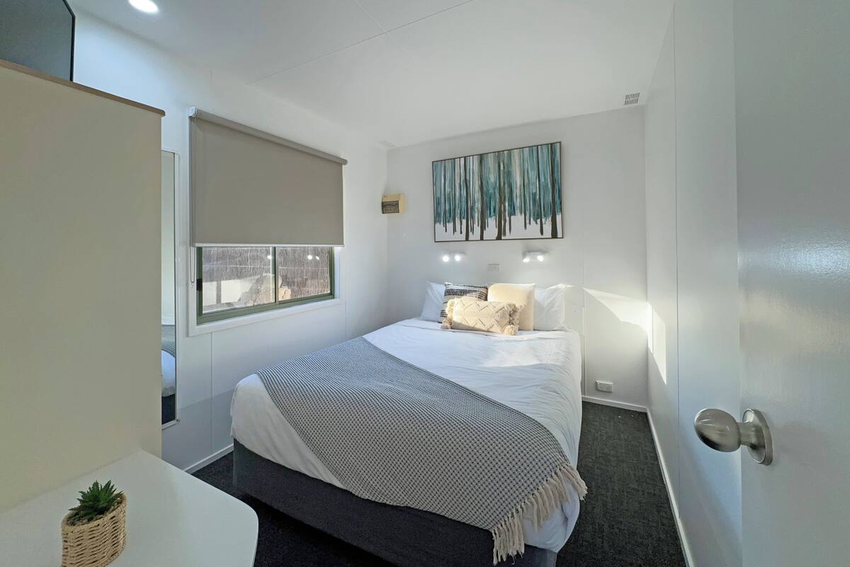 Quarto moderno com cama, abajures, janela com persiana e uma obra de arte pendurada na parede.