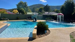 Una piscina con fuente, rodeada de un área ajardinada con un pabellón y vistas a un paisaje montañoso.