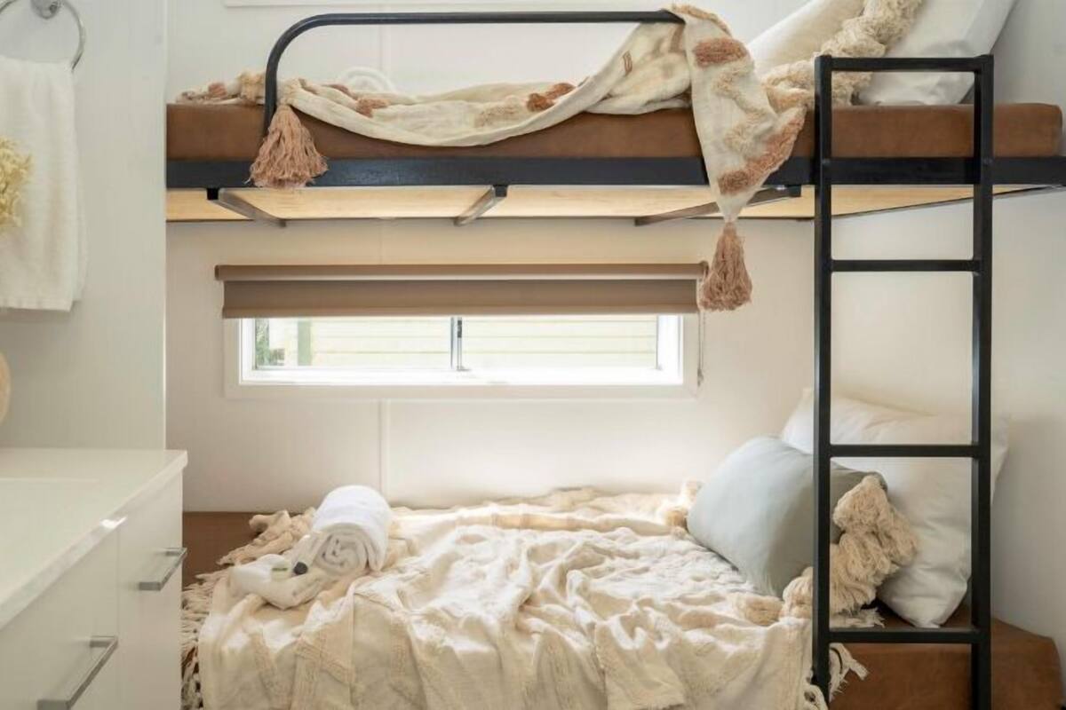 Quarto com beliche, mesa de cabeceira e um vaso com flores secas.