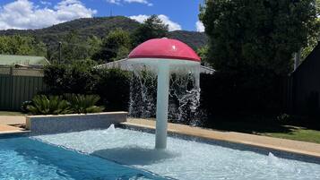 Una piscina con fuente de agua y un toldo rojo.