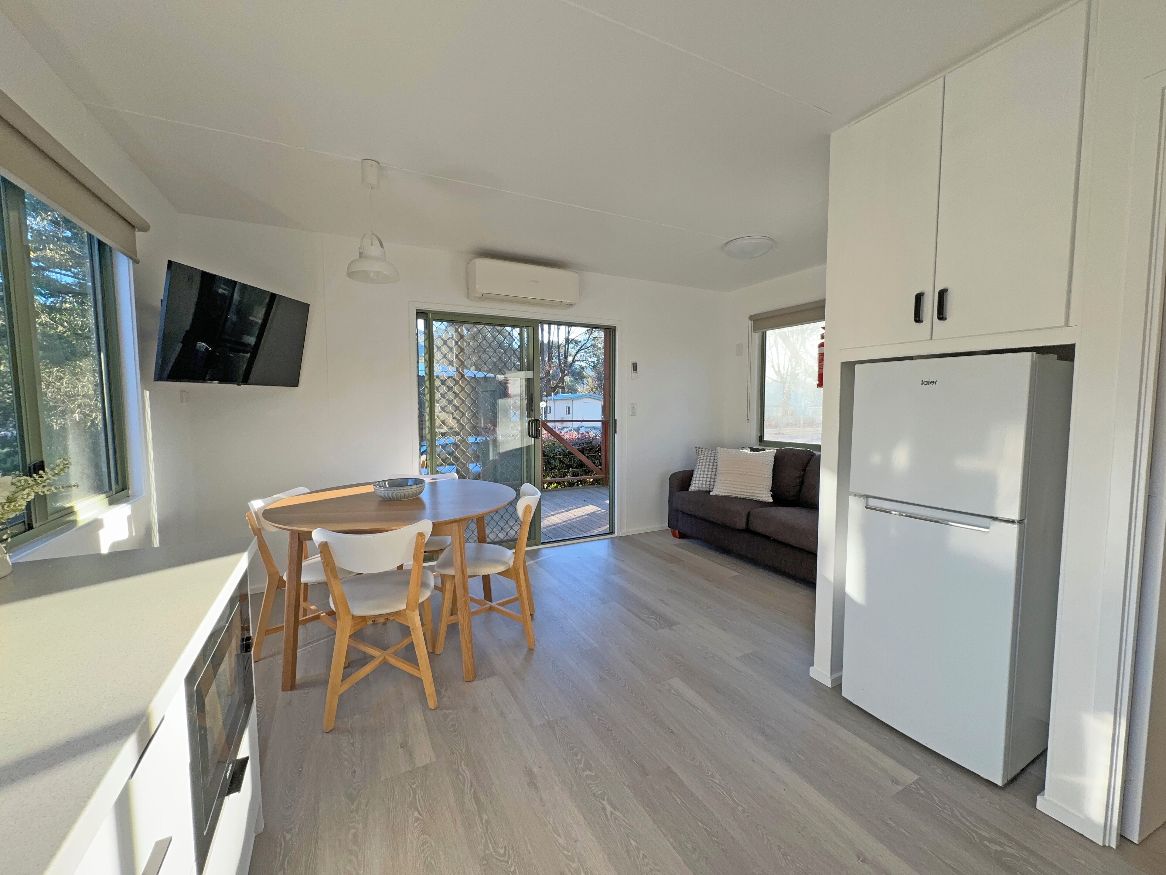 A modern kitchen with a dining area, a sofa, and a TV mounted on the wall.