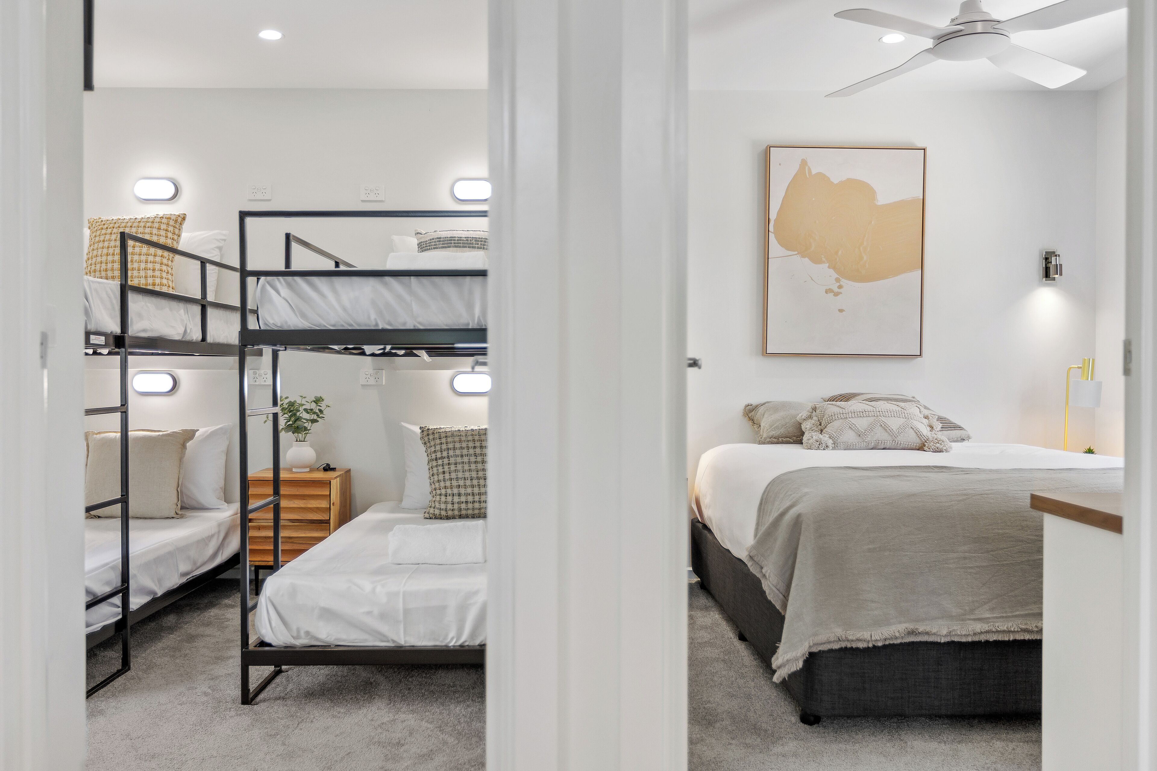 A bunk bed room with a single bed, a wooden nightstand, and a wall-mounted light fixture.
