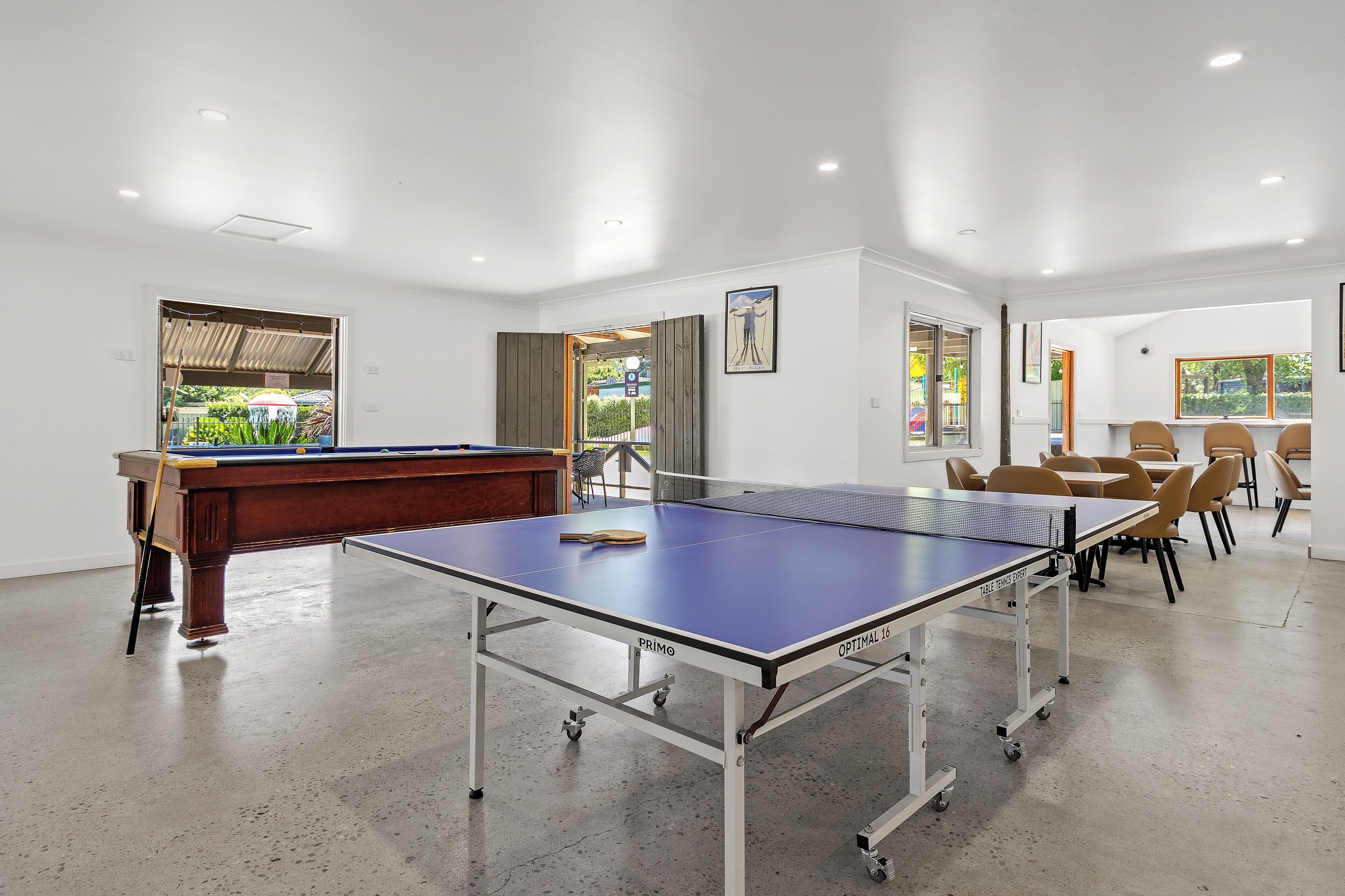 A room with a ping pong table, a pool table, and a dining area with chairs and tables.