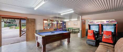 A pool table in a room with arcade games and a couch.